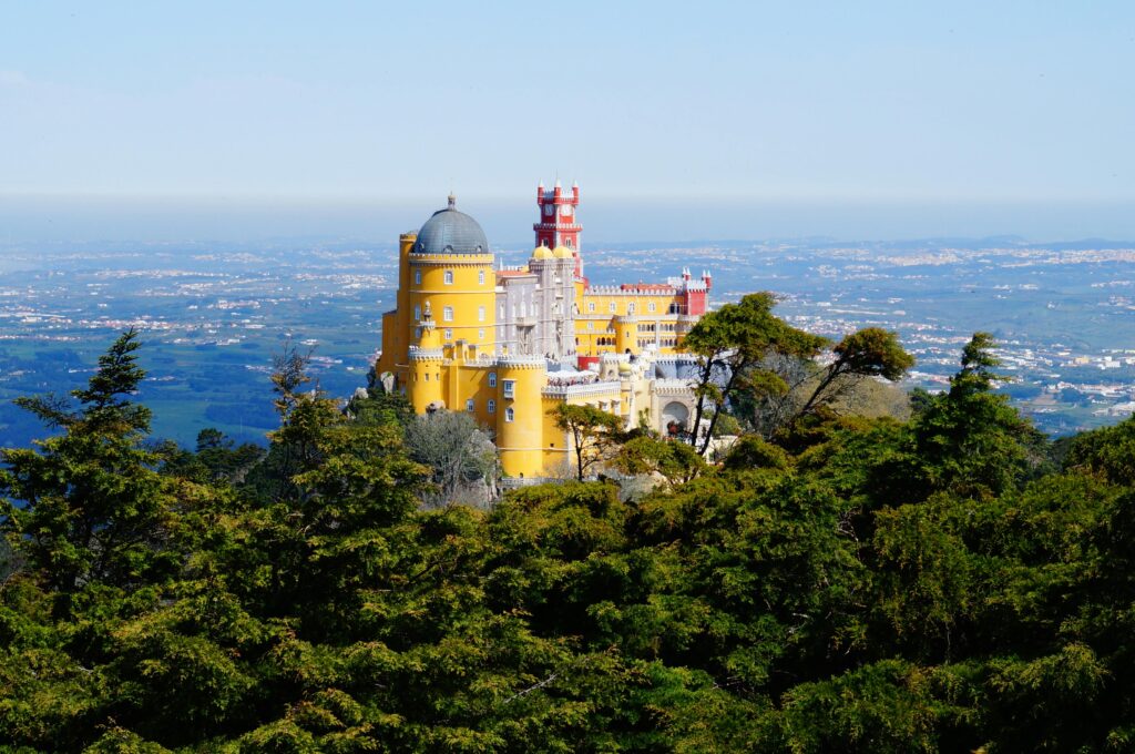 Pena Palace in Sintra, Portugal, sits atop a hill surrounded by trees, overlooking the landscape.